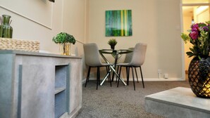 A modern living room with a grey sofa, a coffee table, and a dining area with a glass table and chairs. There is a TV mounted on the wall and a painting above the dining table. - 1br, Balcony, Cityview, Office, Ws98 (London)