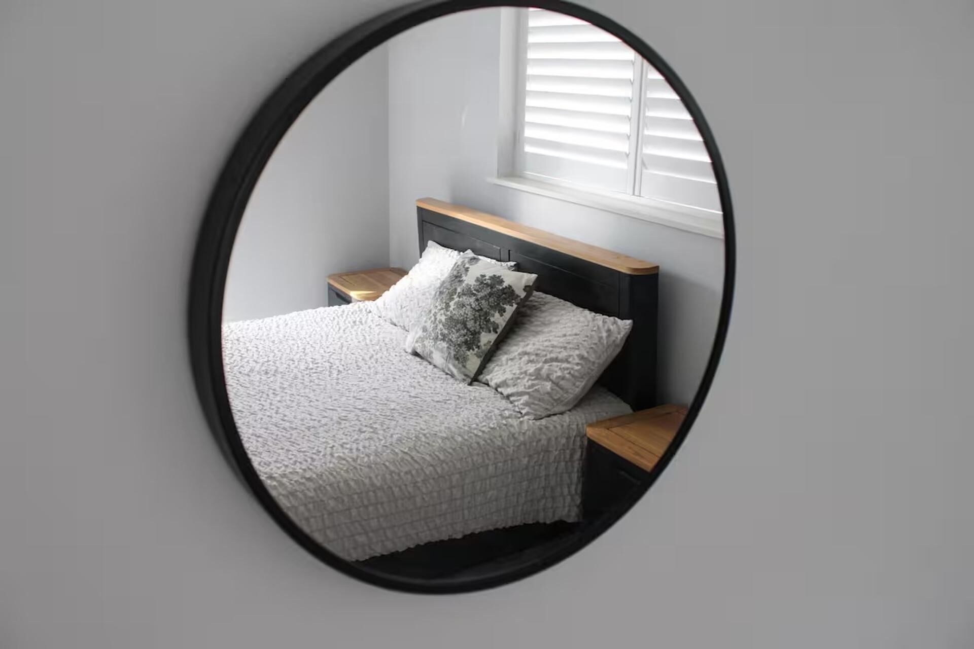 Un dormitorio con cama, dos mesitas de noche, una ventana con persianas y un espejo en la pared.