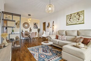 Sala de estar com sofá, mesa de centro e objetos decorativos. Há também uma área de jantar com cadeiras e mesa.