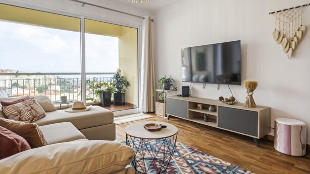 A modern living room with a sofa, TV, and a balcony with plants. - Aura Serena by Madeira Sun Travel (Santa Cruz)