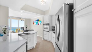 A modern kitchen with white cabinetry, a stainless steel refrigerator, and a large island with a sink.
