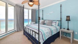A bedroom with a bed, a ceiling fan, a nightstand, and a view of the ocean.