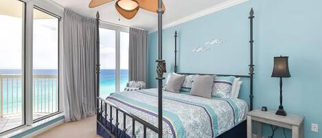 A bedroom with a bed, a ceiling fan, a nightstand, and a view of the ocean.