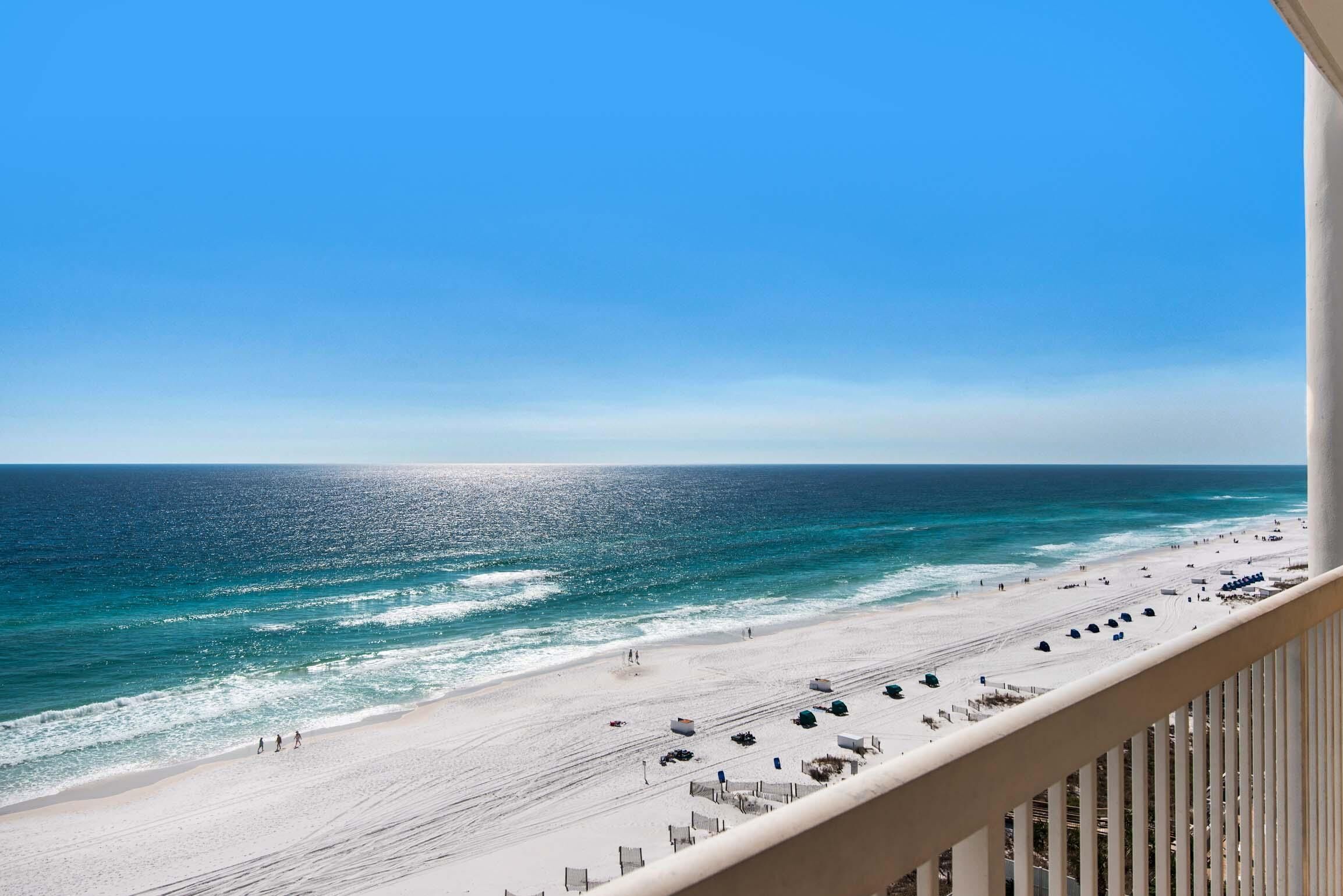 A beach view from a balcony with a clear sky, sandy beach, and ocean.