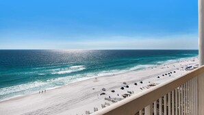 A beach view from a balcony with a clear sky, sandy beach, and ocean.