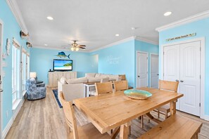 A room with a wooden dining table, beige sofa, and a television on a cabinet.