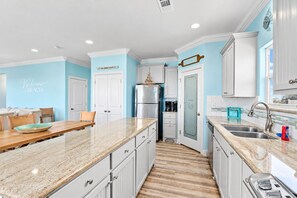 A kitchen with white cabinetry, a granite countertop, and a stainless steel refrigerator. - 2nd Row Crystal Beach Home | Steps Away | Sleeps 18 (Crystal Beach)