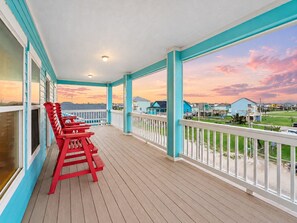 A covered porch with a view of houses and a sunset.