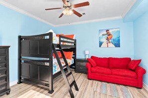 A room with a bunk bed, a red sofa, a ceiling fan, and a painting on the wall.