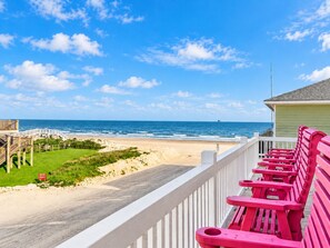 A beach view from a balcony with a wooden deck and red chairs.