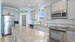 A kitchen with white cabinets, a granite countertop, stainless steel appliances, and a tiled backsplash. - 2nd Row Crystal Beach Home | Steps Away | Sleeps 18 (Crystal Beach)