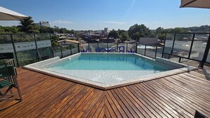 Una piscina en la azotea con cubierta de madera, rodeada de barandillas de vidrio y vistas despejadas del paisaje urbano.