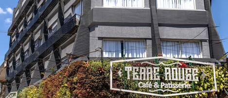 A building with a cafe and pastry shop on the ground floor, featuring outdoor seating and a sign reading "Terre Rouge Cafe & Patisserie".