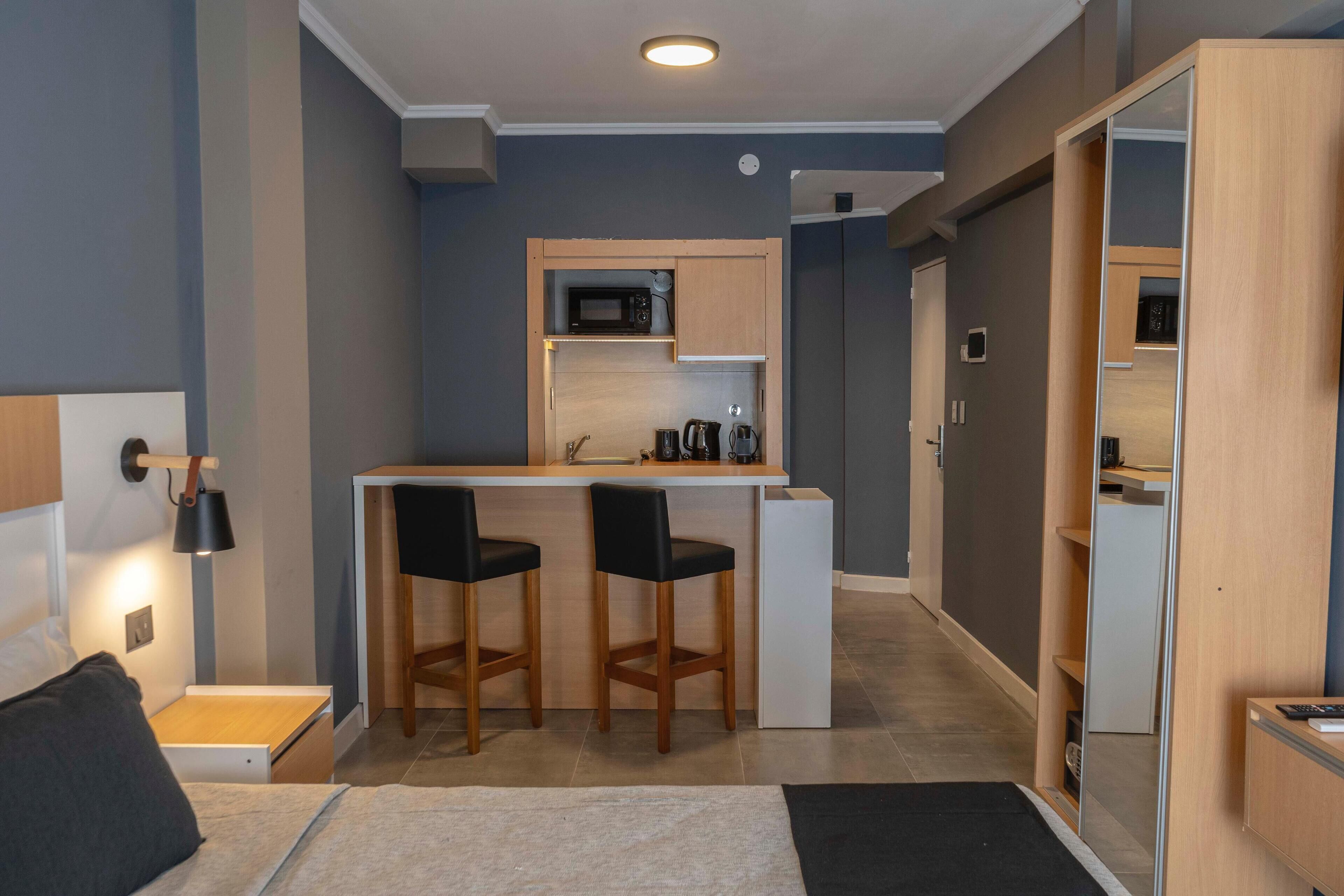 A compact hotel room with a kitchenette, a bed, a desk with two chairs, and a wardrobe.