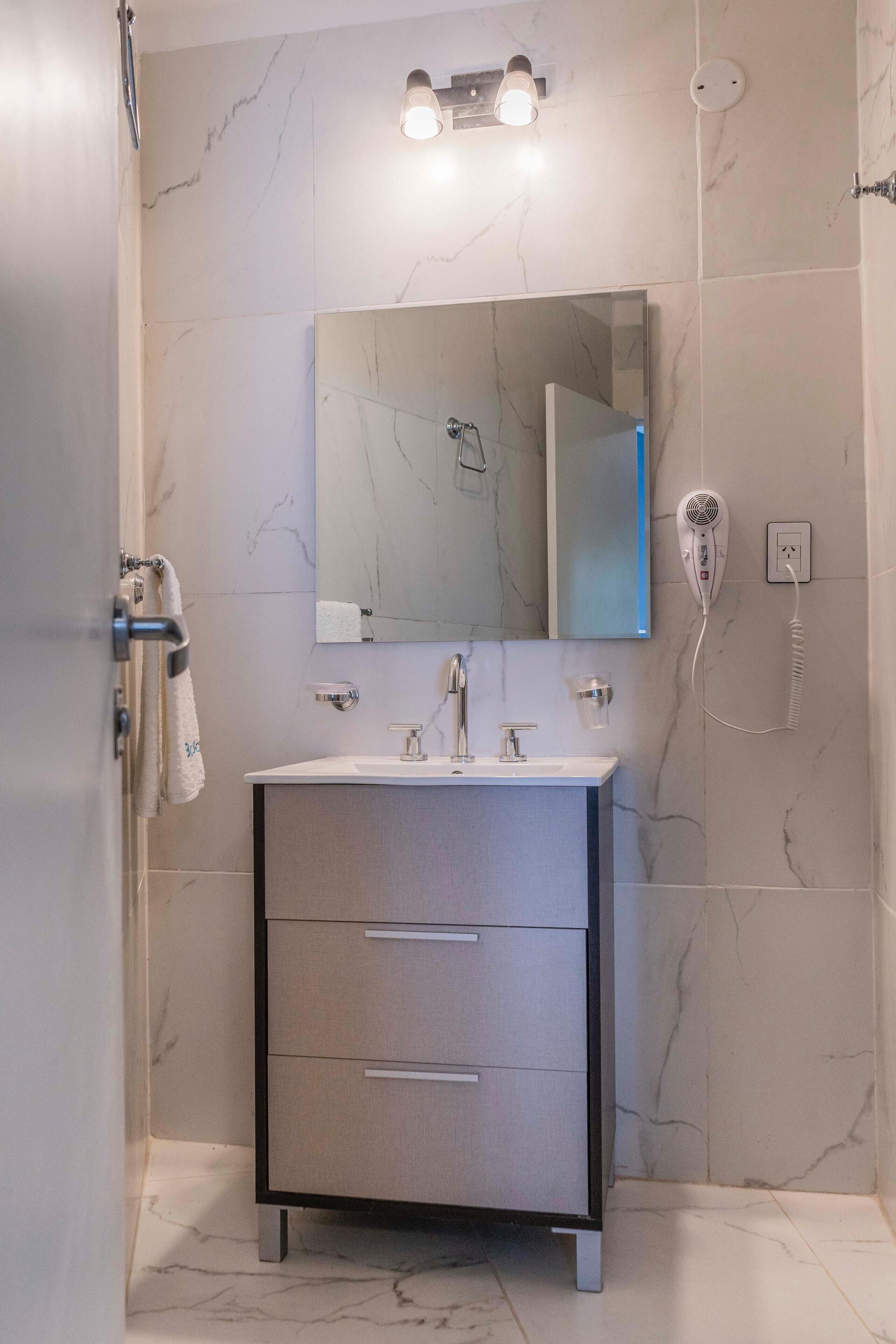 Un baño con pared de mármol, tocador con espejo, secador de pelo y perchero para toallas.