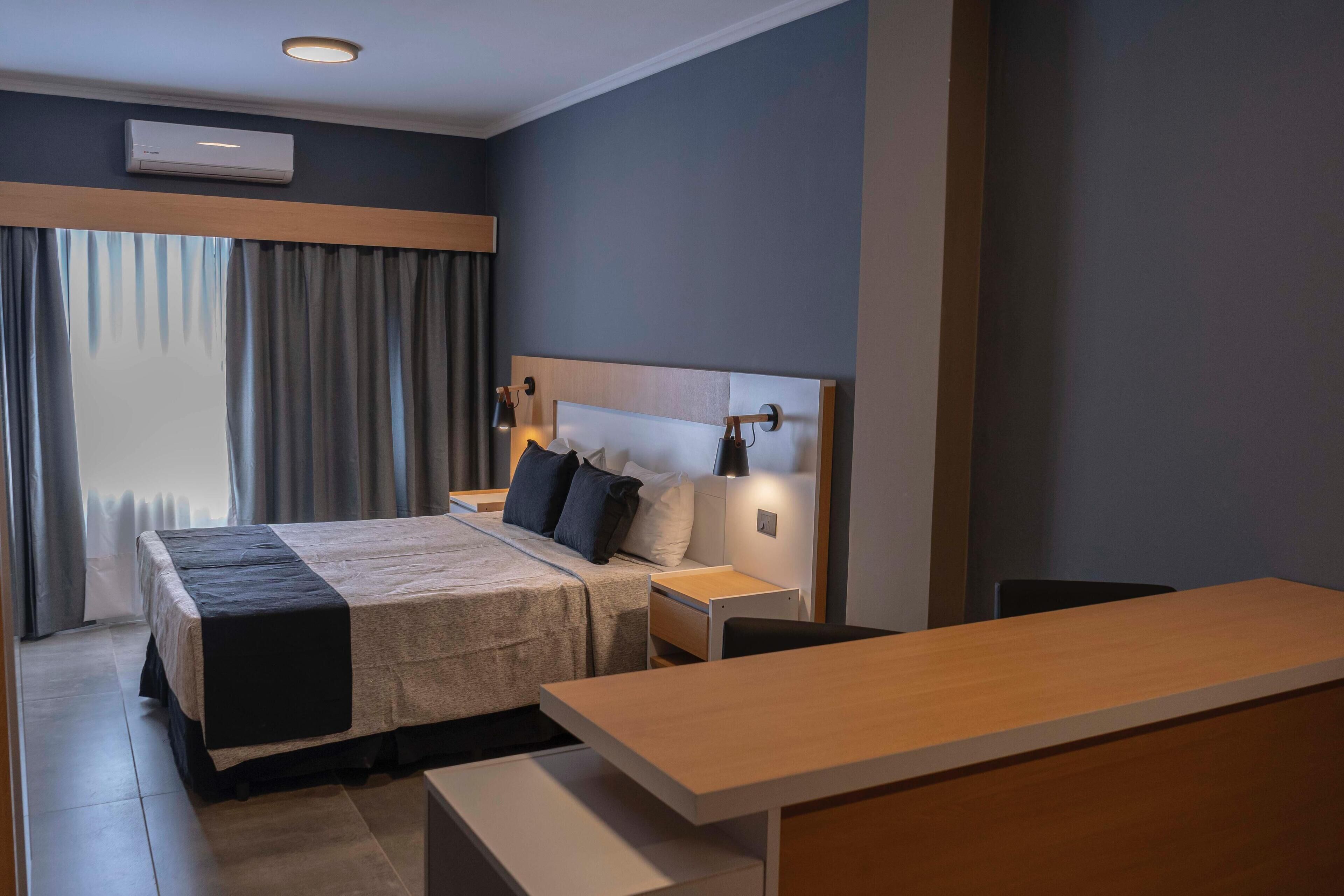 Une chambre d’hôtel moderne équipée d’un lit, de tables de chevet, d’un bureau et d’une fenêtre avec des rideaux.