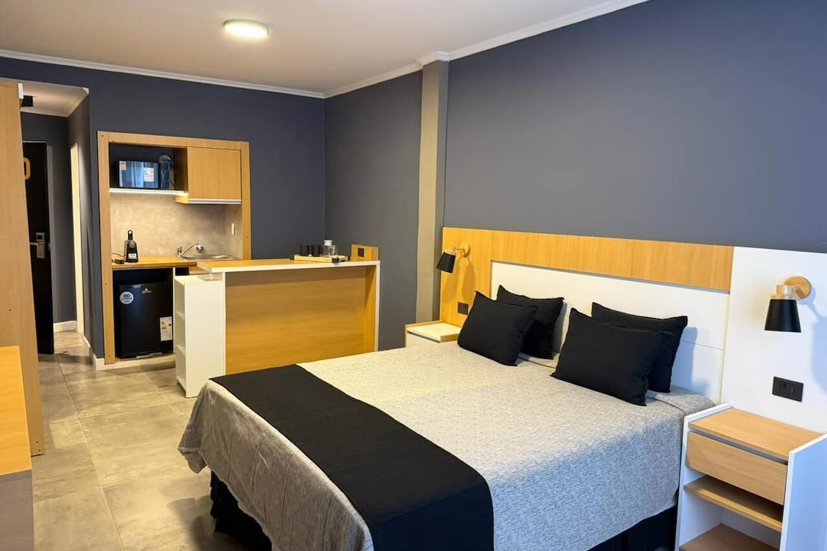 Ein modernes Hotelzimmer mit einem großen Bett, Nachttischen, einem fest eingebauten Schreibtisch und einer Küchenzeile.
