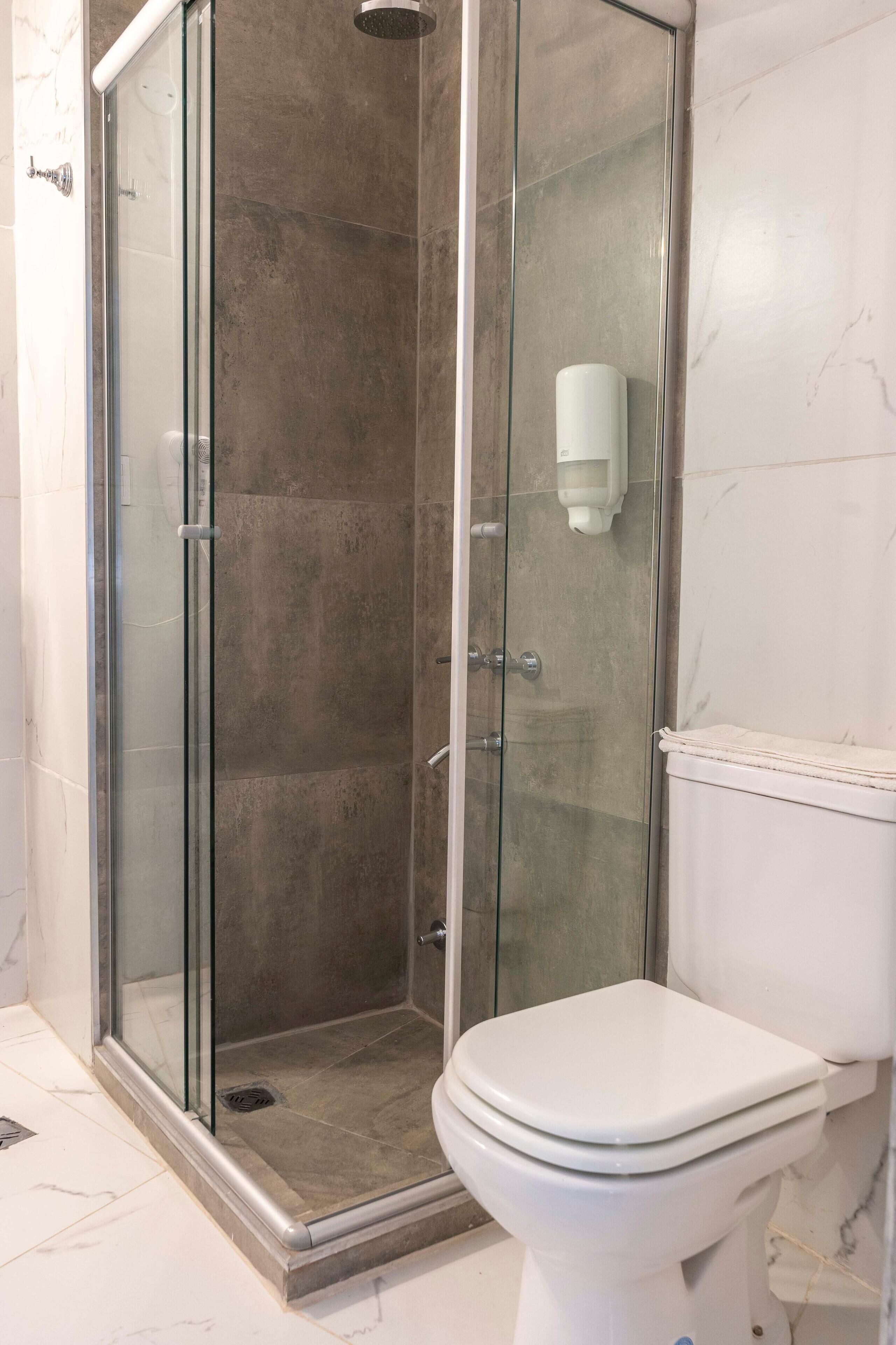 Une salle de bain avec une douche à parois de verre, des toilettes et un distributeur de savon fixé au mur.
