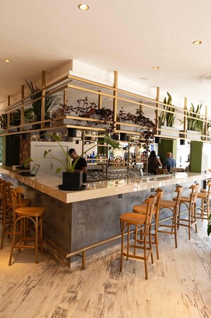 Een moderne bar met een marmeren aanrecht, houten barstoelen en verschillende planten.