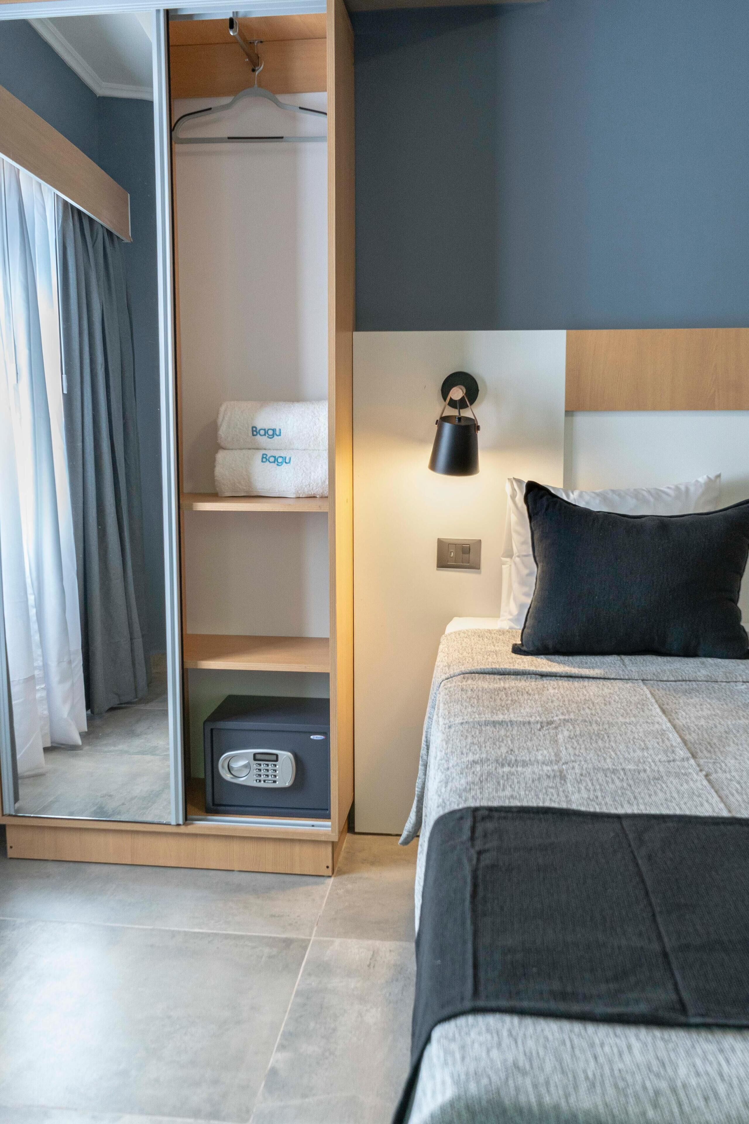 A hotel room with a bed, a bedside table, a nightstand, a wardrobe, and a wall-mounted lamp.