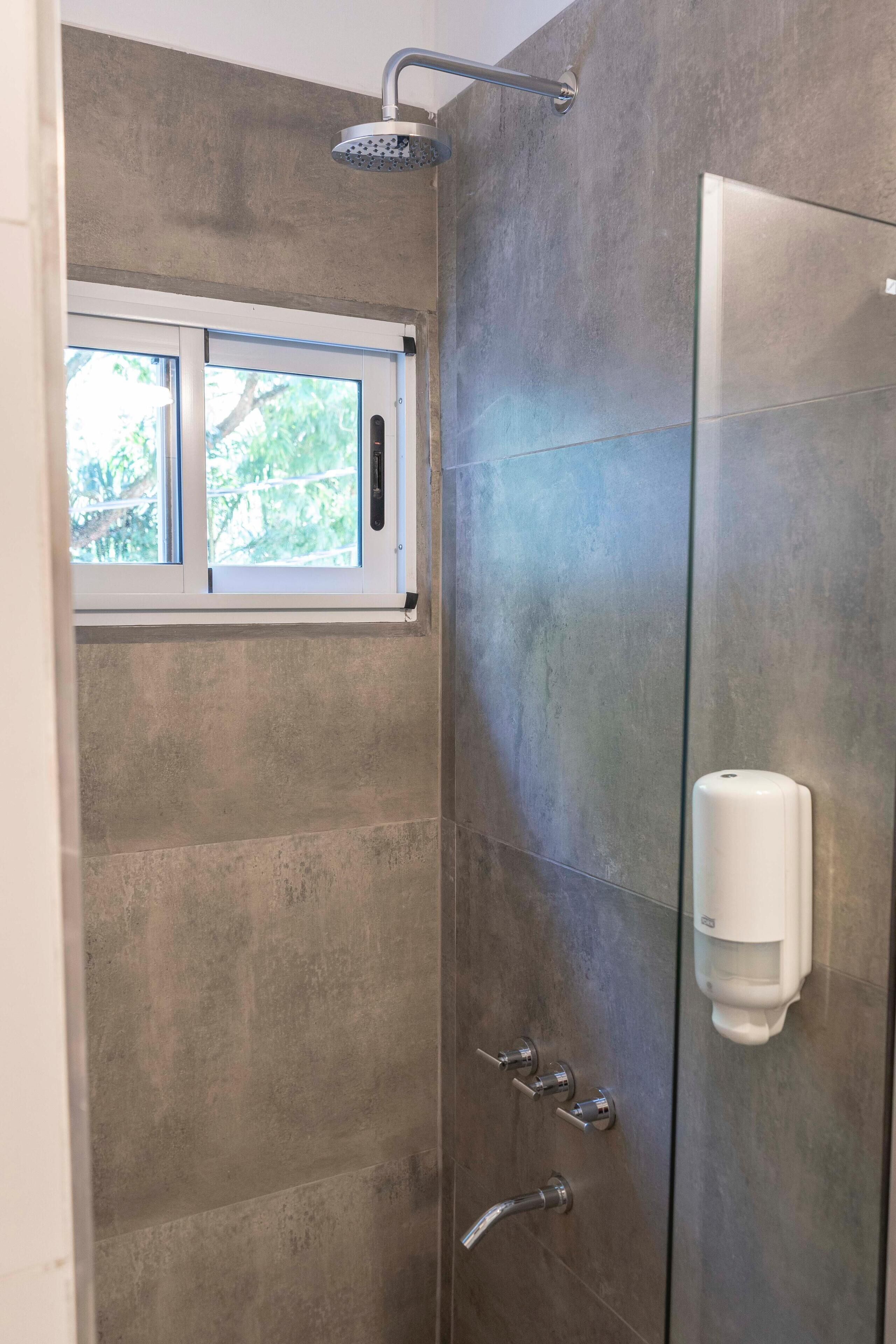 A shower with a glass door, a window, and a soap dispenser.