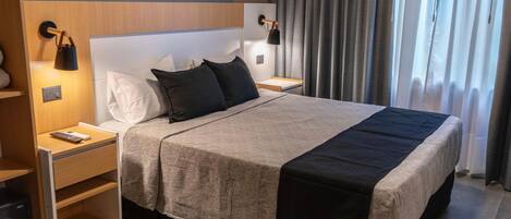 Een moderne hotelkamer met een groot bed, nachtkastjes, een lamp en uitzicht op het groen door gordijnen.