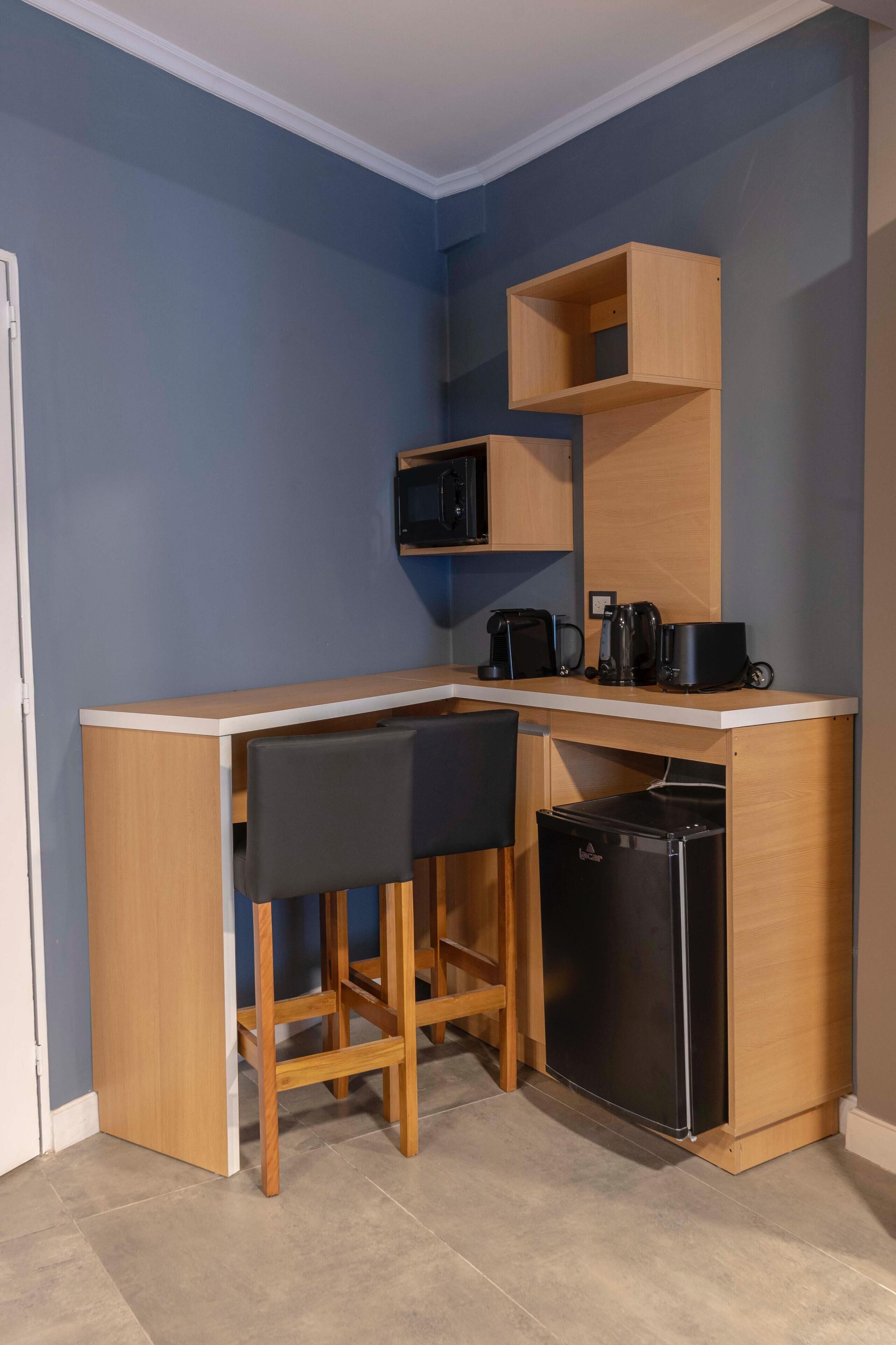 Une cuisine de taille réduite, dotée d’un plan de travail en bois, d’un réfrigérateur noir et d’un four à micro-ondes placé au-dessus.