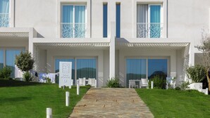 A modern hotel with a stone pathway leading to a double door entrance, white outdoor furniture, and a clear view of the surrounding landscape. - Stunning Capo Falcone Charming Apartments num 5089 (Stintino)