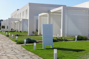 Una hilera de edificios modernos y blancos, con un sendero de piedra que los conduce. Cada edificio tiene un cartel con un número de habitación.