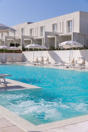 Una piscina con sillas de descanso y sombrillas, rodeada por un edificio moderno con balcones.