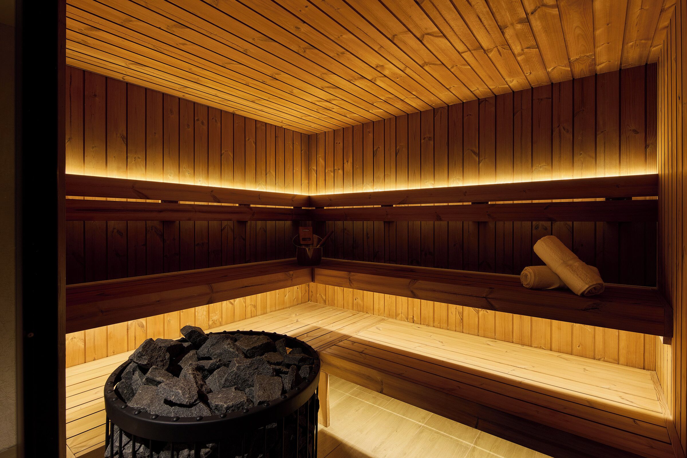Een sauna met houten wanden en banken, een vuurkorf in het midden en een bank met een handdoek.