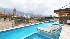 A rooftop swimming pool with lounge chairs, a bar area, and a cityscape view in the background. - Landmark Hotel (Medellín)