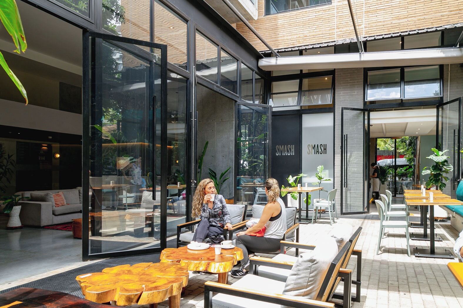An outdoor seating area with tables and chairs, a glass wall, and a building with 'SMASH' signage.