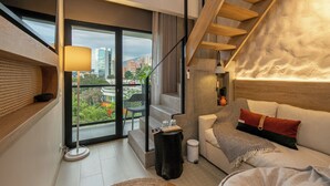 A modern living room with a sofa, a coffee table, a lamp, and a view of the city through large windows. - Landmark Hotel (Medellín)