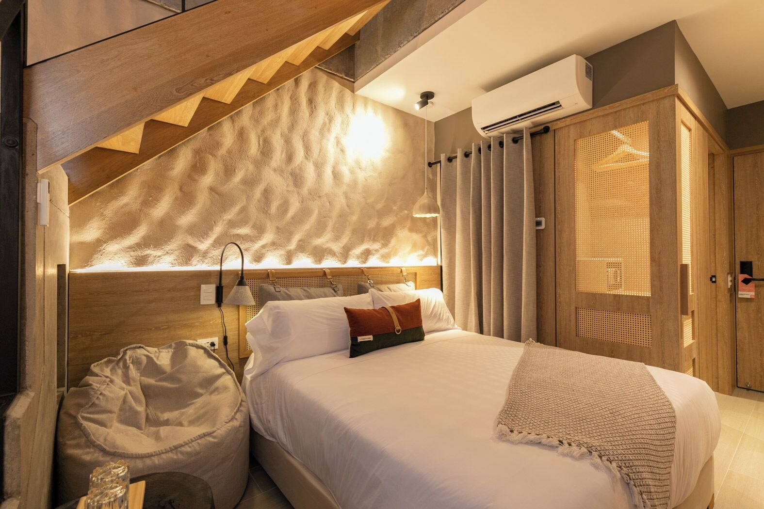 A bedroom with a bed, a headboard, a wooden staircase, an air conditioning unit, and a wardrobe.