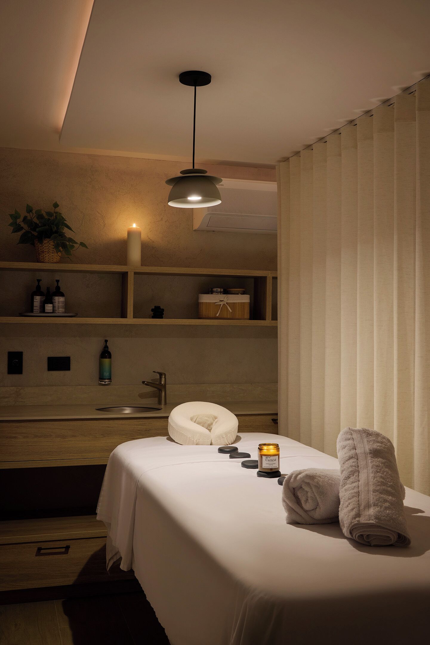 A bedroom with a bed, bedside table, candles, and a hanging light fixture.