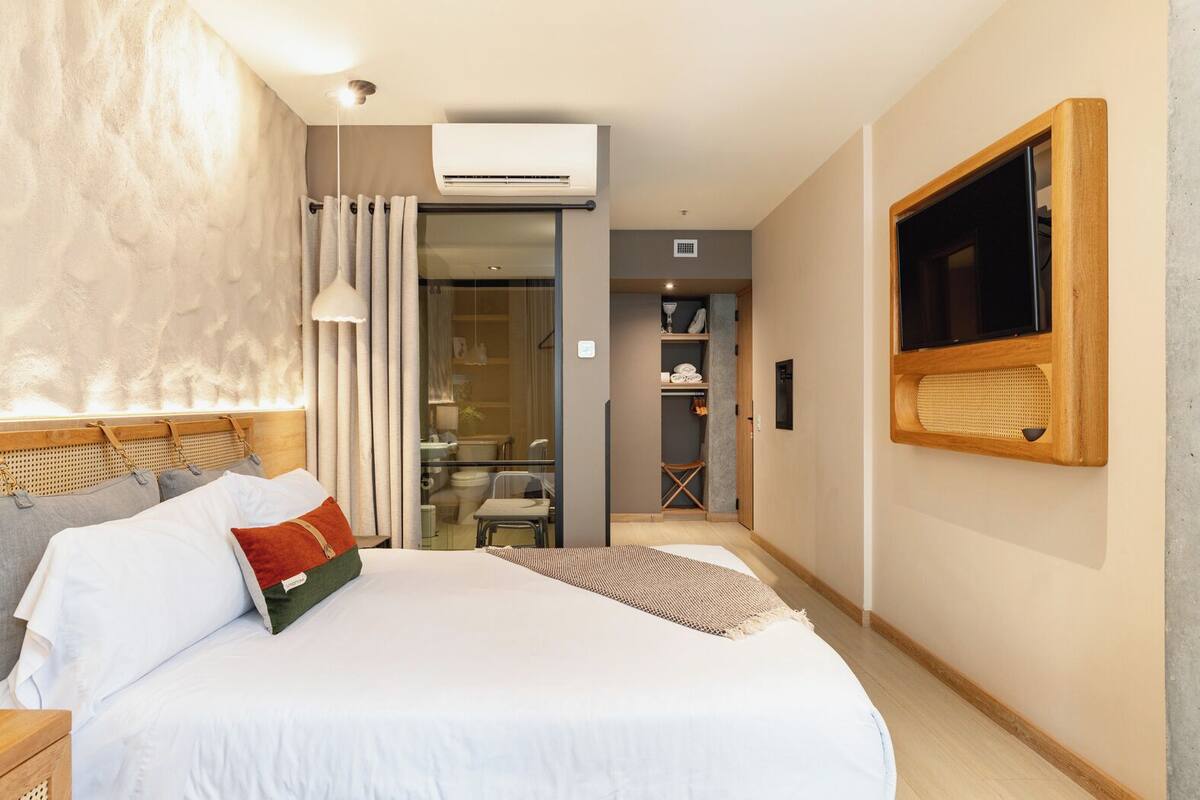 A modern hotel room with a large bed, a television mounted on the wall, and a sliding glass door leading to a bathroom.