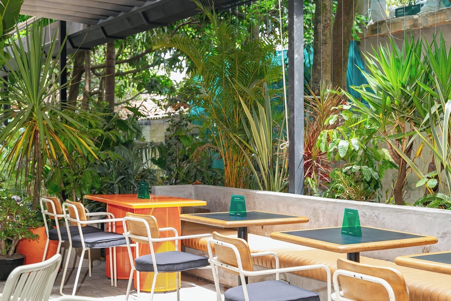 An outdoor patio with tables and chairs, surrounded by various plants and greenery.