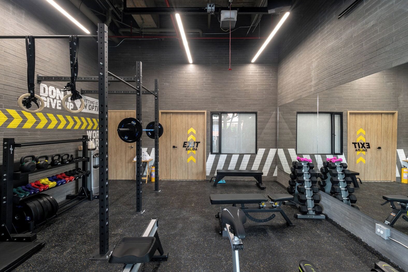 Uma academia com equipamentos de musculação, bancos e um espelho grande.