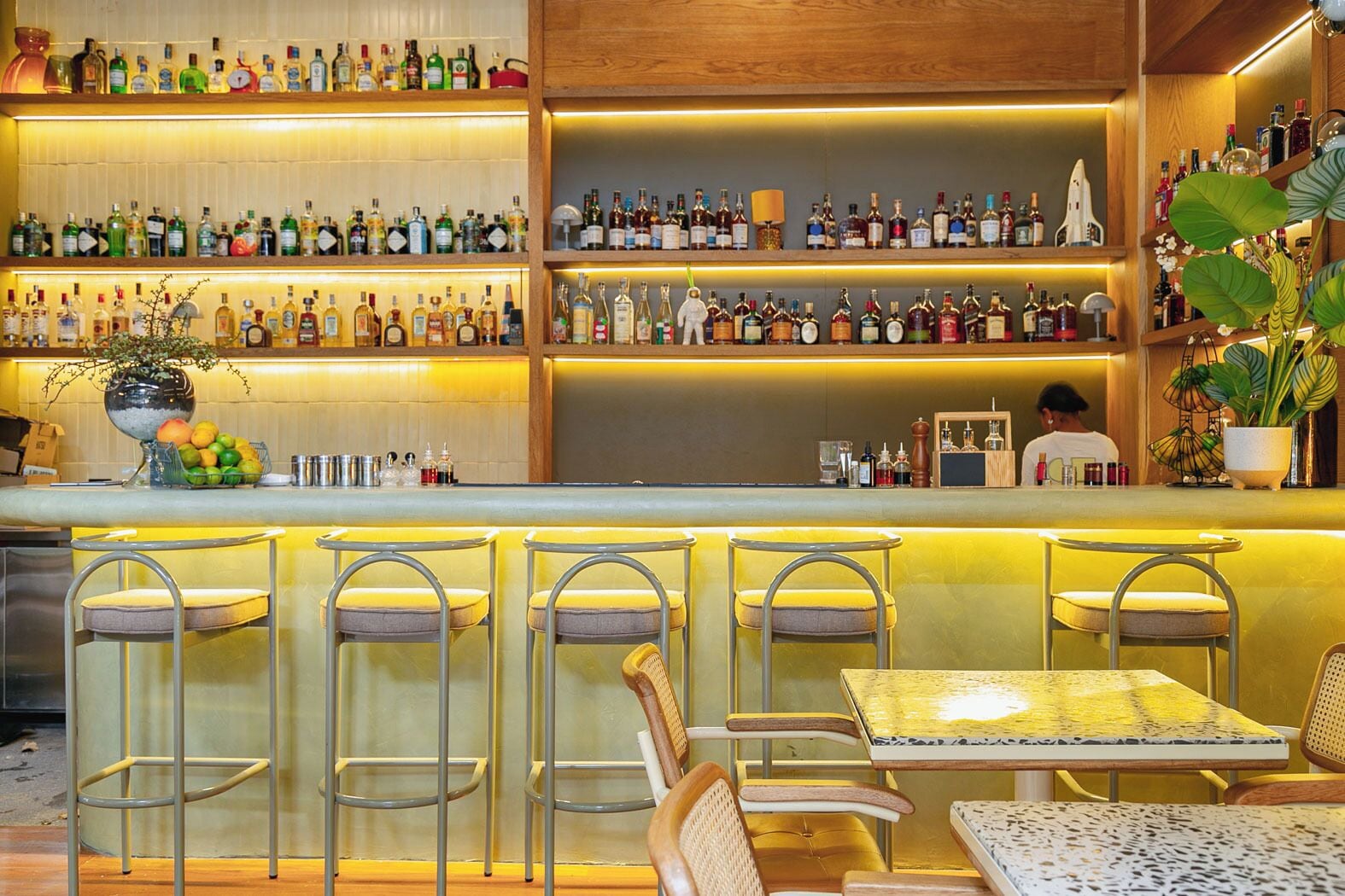 Zona de bar con varios estantes de botellas de licor, taburetes y barra.