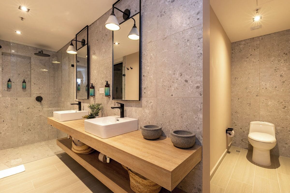A modern bathroom with two sinks, a large mirror, and a toilet.