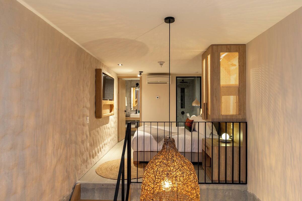 A modern interior with a staircase leading to a bedroom. There is a hanging light fixture in the foreground.