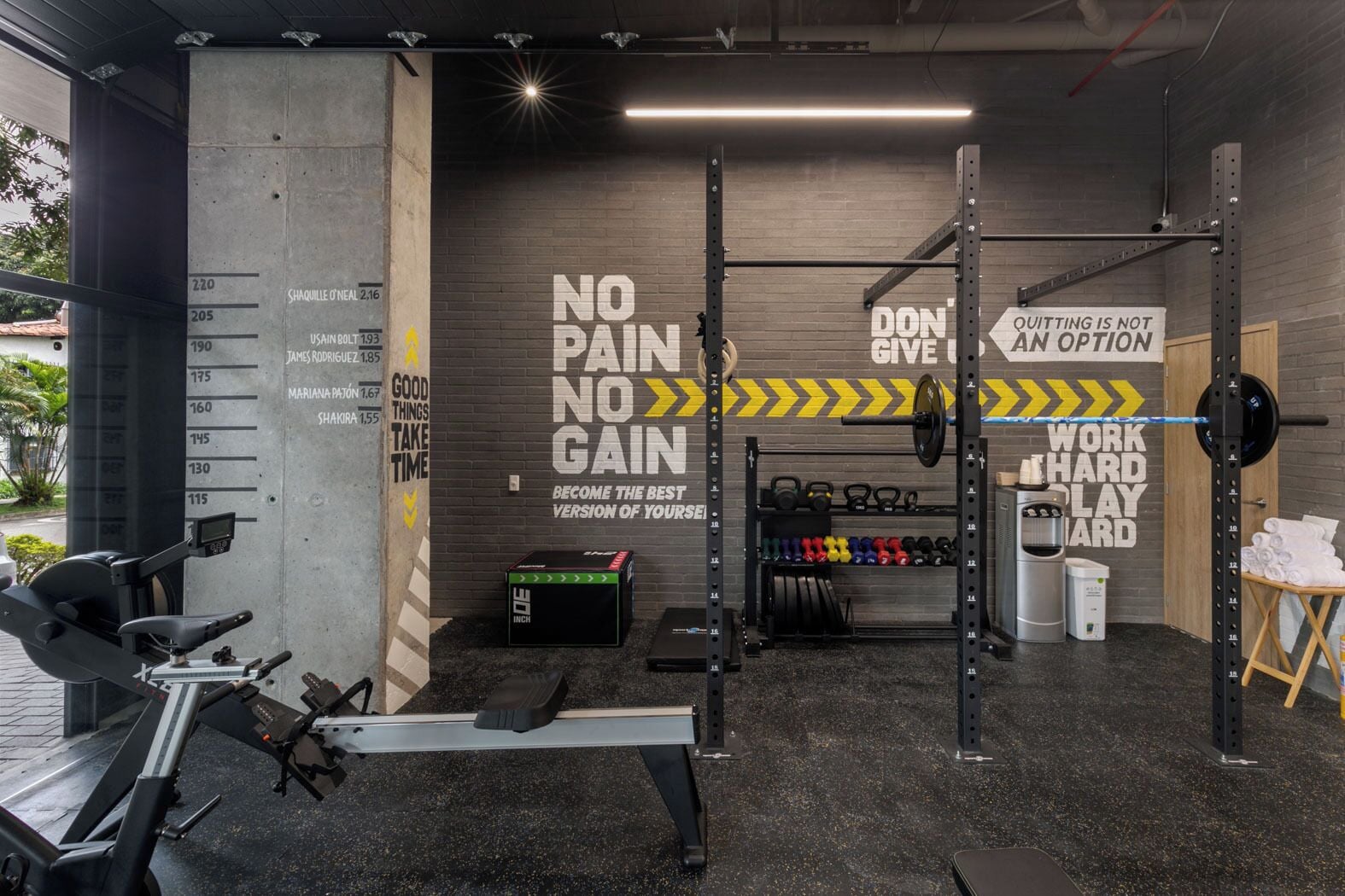 A gym with motivational wall art, weightlifting equipment, and a rowing machine.