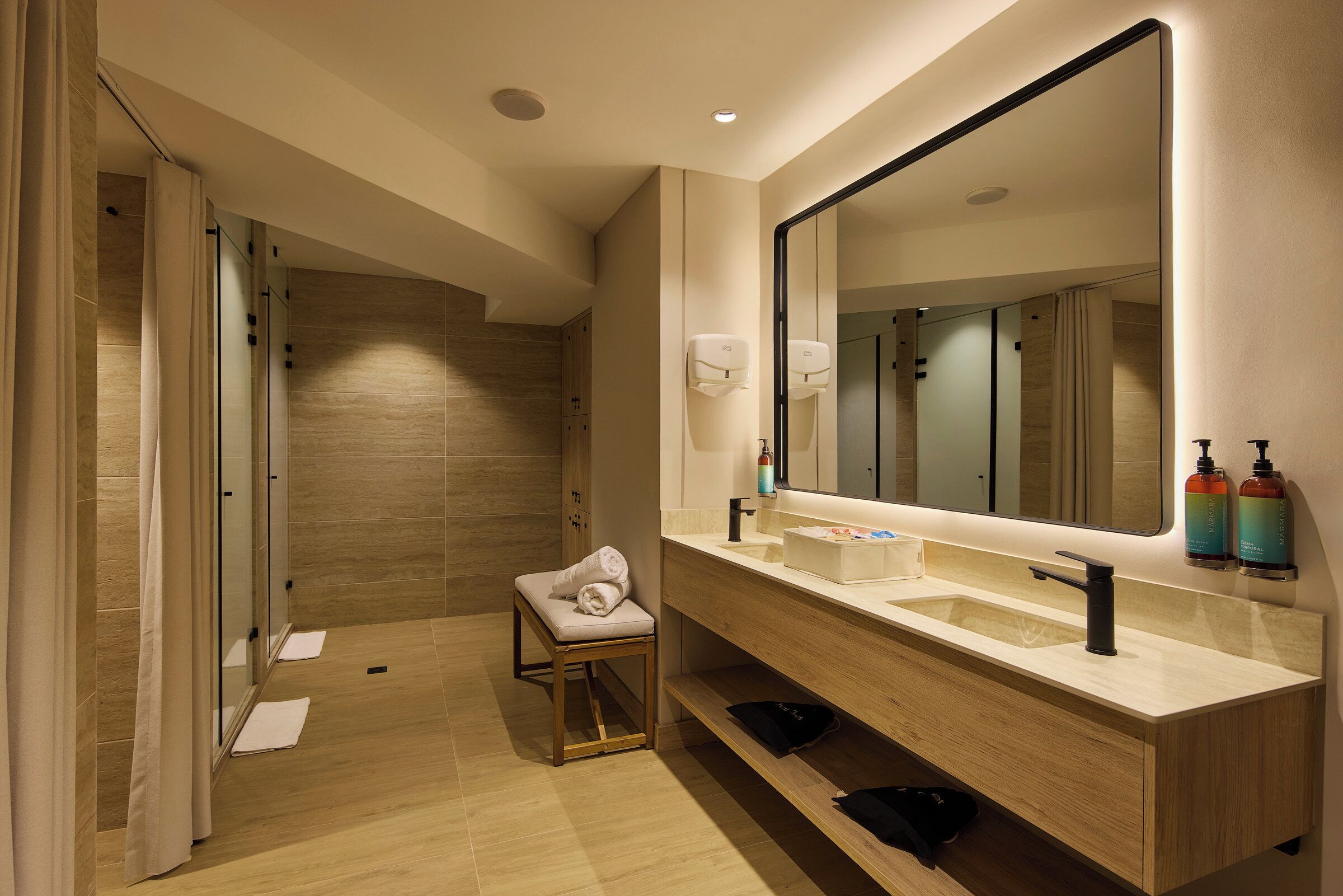 A modern bathroom with a large mirror, dual sinks, and a shower area.