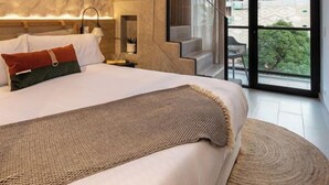 A modern bedroom with a large bed, a wooden staircase, and a city view through the glass door. - Landmark Hotel (Medellín)