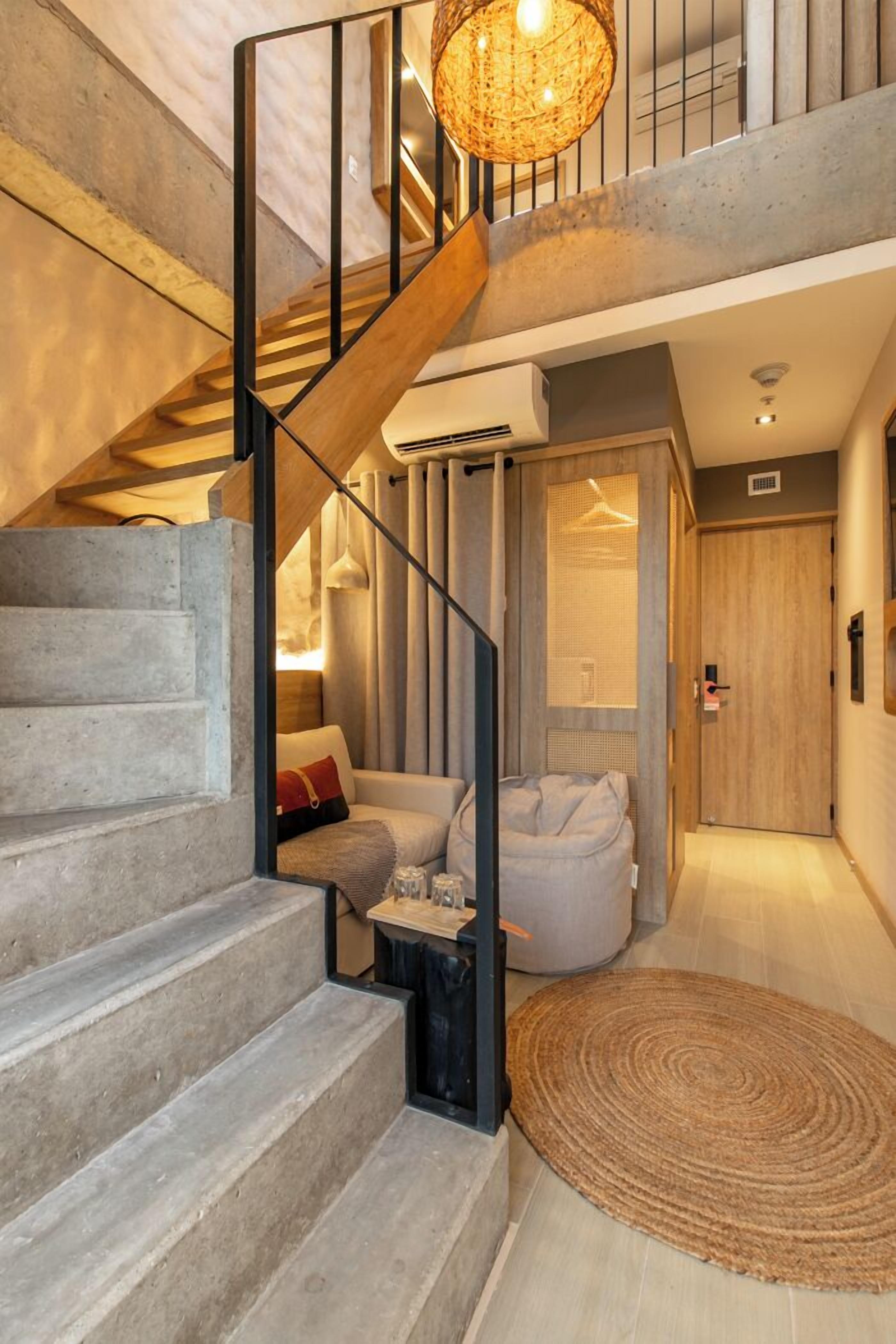 Una escalera con detalles de madera y barandillas negras que conduce a una habitación con un sofá blanco y un tapiz redondo tejido.