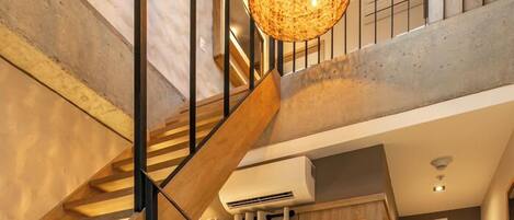 Una escalera con detalles de madera y barandillas negras que conduce a una habitación con un sofá blanco y un tapiz redondo tejido.