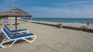 Una playa con sillones de baño y una sombrilla de paja.