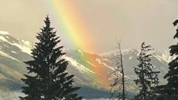 Un paysage de montagne avec un arc-en-ciel, des arbres et un lac.