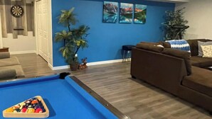 Una sala de estar con mesa de billar, un sofá marrón y una pared de acento azul.